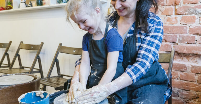 Young mom and her little daughter learning pottery on a pottery wheel.